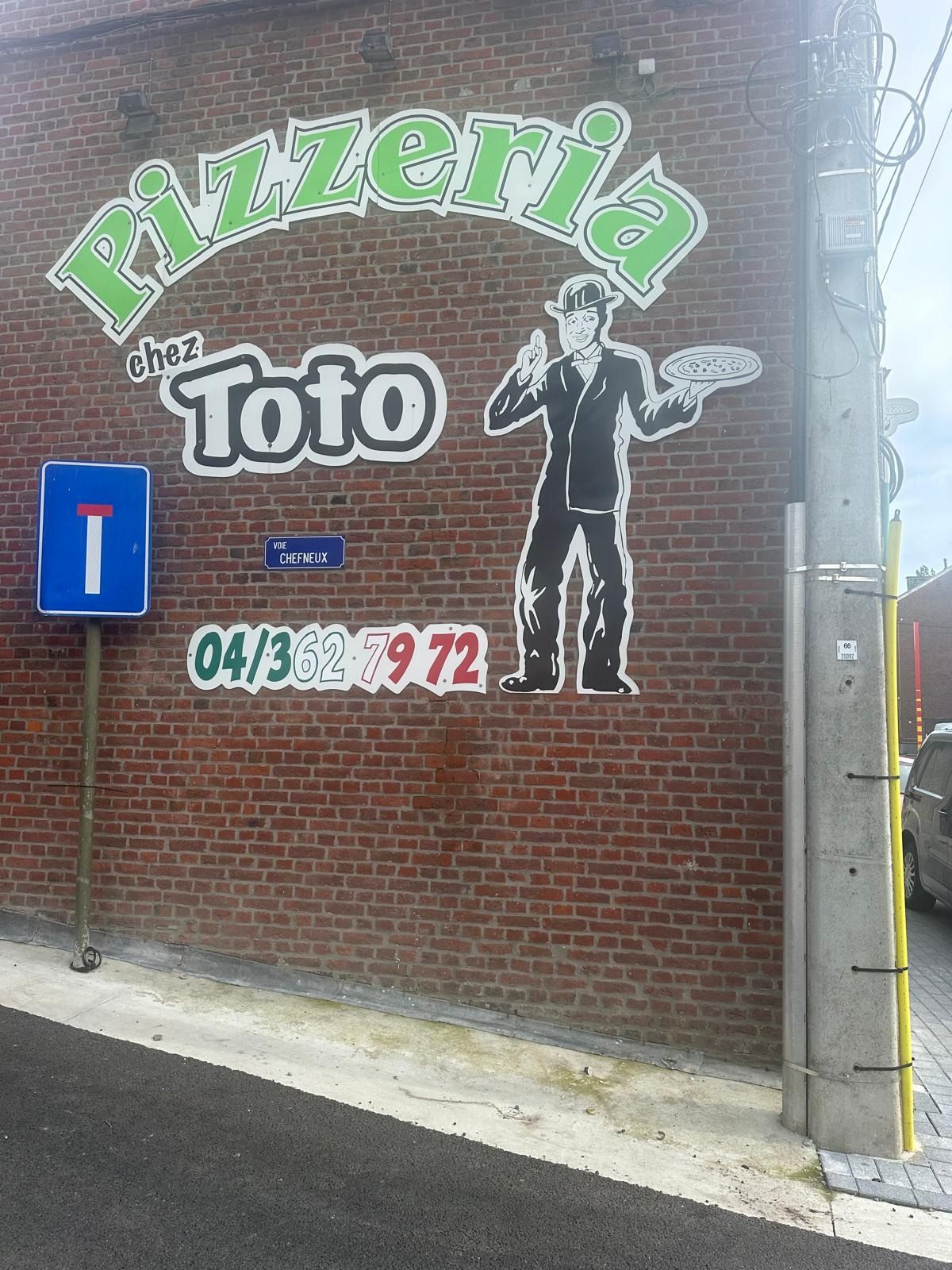 Le mur de briques de la pizzeria, avec l’enseigne peinte et Toto